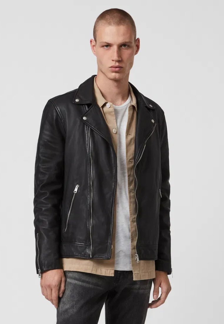 Schwarze Leder-Bikerjacke mit asymmetrischem Reißverschluss, Reverskragen und silbernen Beschlägen. Tragen über einem beigen Button-up-Hemd.