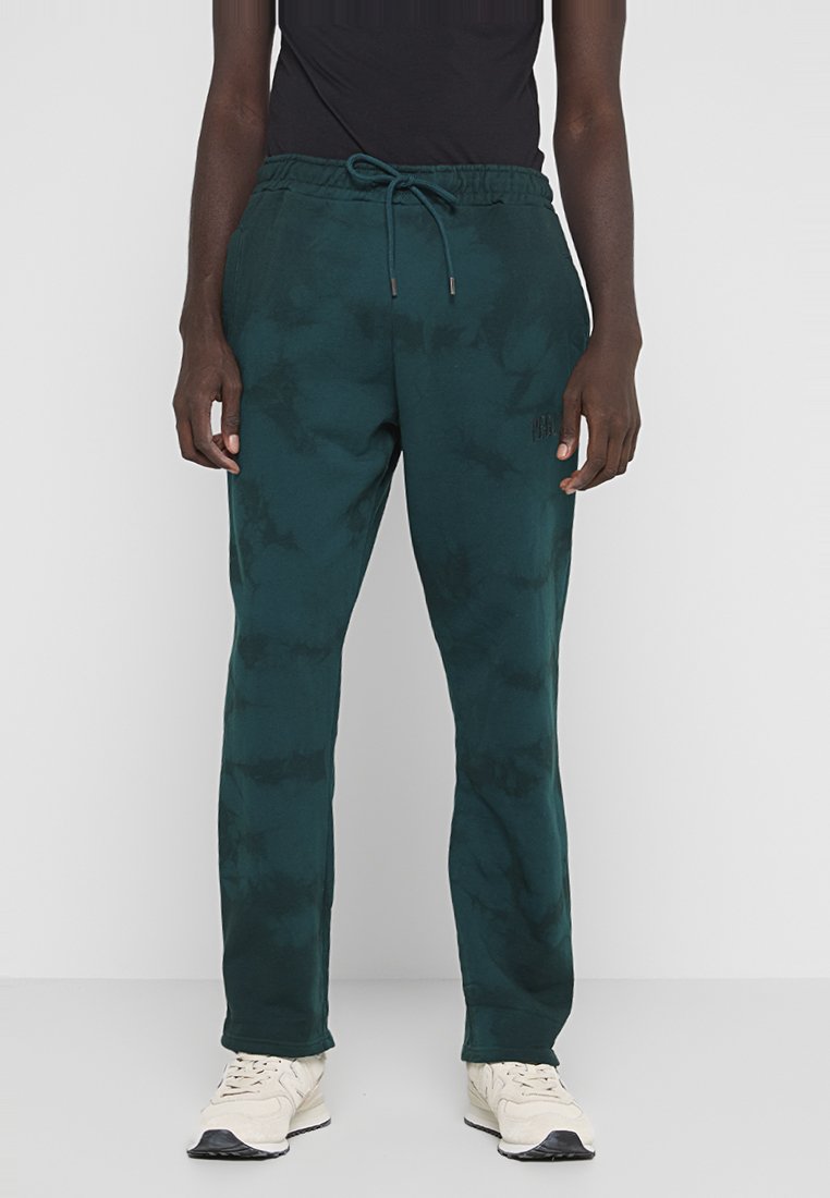 Grüne Tie-Dye-Sweatpants mit einem Kordelzugbund, die eine lockere Passform und eine weiche Textur aufweisen, kombiniert mit hellen Sneakers.