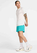 Helles graues Sport-T-Shirt mit kurzen Ärmeln, kombiniert mit türkisfarbenen Shorts und weißen Laufschuhen. Enthält Nike-Logos auf der Bekleidung.