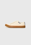 Weiße Leinensneaker mit einer Gummisohle, ausgestattet mit goldenen Ösen, einem marineblauen Akzent an der Ferse und einer abgerundeten Spitze.