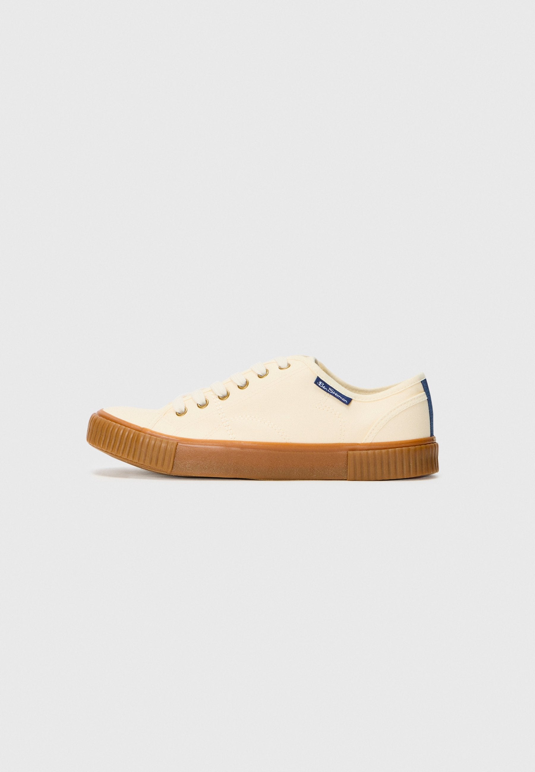 Weiße Leinensneaker mit einer Gummisohle, ausgestattet mit goldenen Ösen, einem marineblauen Akzent an der Ferse und einer abgerundeten Spitze.