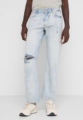 Helle blaue Jeans mit lockerem Schnitt, mit Rissen am linken Knie und einem klassischen Fünf-Taschen-Design. Getragen mit beigen Sneakern.