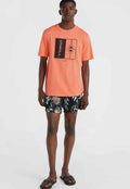 Koralle T-Shirt mit schwarzem Grafikdesign, kombiniert mit schwarzen Shorts mit buntem tropischen Muster. Modell trägt schwarze Flip-Flops.