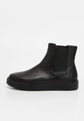 Schwarze Chelsea-Stiefel aus Leder mit strukturierter Oberfläche, elastischen Seitenpaneelen und dicker schwarzer Sohle. Markenetikett an der Seite sichtbar.