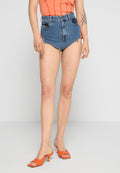 Blaue High-Waist-Jeansshorts mit fransigem Saum, kombiniert mit einem orangefarbenen Oberteil und orangefarbenen Absatzschuhen. Glatte Denim-Oberfläche sichtbar.