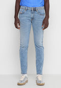 Person trägt hellblaue Slim-Fit-Jeans, ein blaues Hemd und silberne Sneaker mit weißen Schnürsenkeln vor einem einfarbigen Hintergrund.