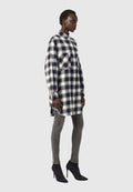 Schwarz-weiße karierte Oversized-Hemdblusenkleid mit Kragen und seitlichen Schlitzen, kombiniert mit eng anliegenden grauen Jeans und schwarzen, hochhackigen Stiefeletten.