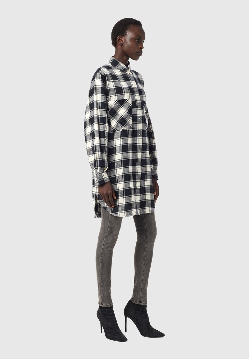 Schwarz-weiße karierte Oversized-Hemdblusenkleid mit Kragen und seitlichen Schlitzen, kombiniert mit eng anliegenden grauen Jeans und schwarzen, hochhackigen Stiefeletten.