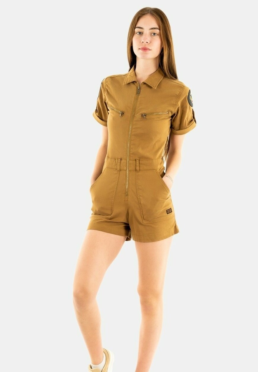 Beige Kurzarm-Overall mit Reißverschluss vorne, zwei Brusttaschen und taillierter Passform. Entworfen mit hochgerollten Ärmeln und einem Patch-Akzent.