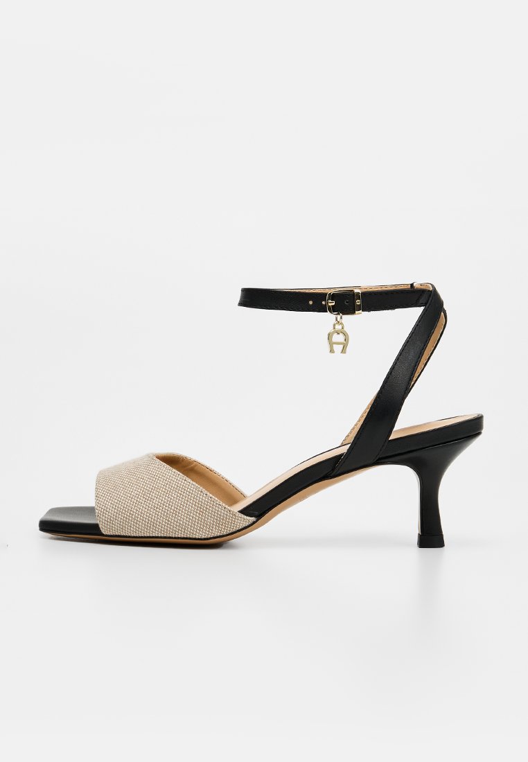 Schwarze und beige Damen-Sandale mit offenem Zehenbereich, mittelhohem Absatz, Knöchelriemen und kleinem goldfarbenem Anhänger am Schnallenverschluss.