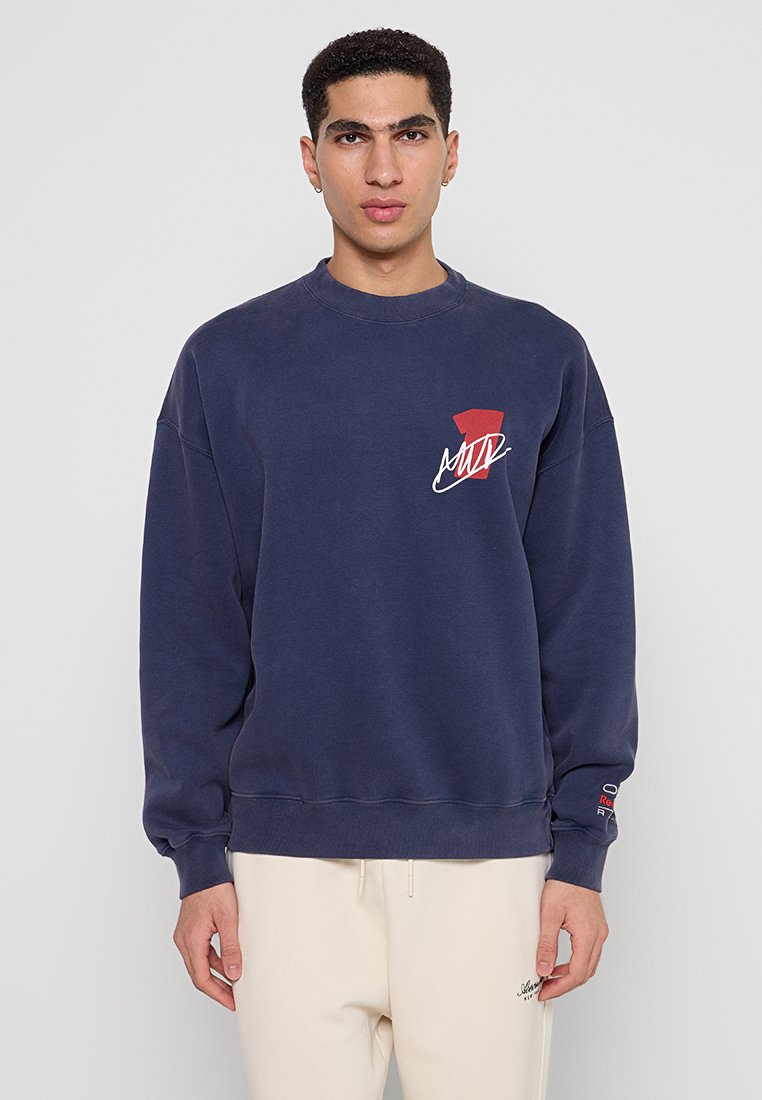 Marineblaues Sweatshirt mit Rundhalsausschnitt, langen Ärmeln und einem rot-weißen Grafikdesign auf der Brust. Mit gerippten Bündchen und Saum.