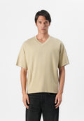 Beige T-Shirt mit kurzen Ärmeln und V-Ausschnitt aus weicher Baumwolle in lockerer Passform, kombiniert mit dunkelblauen Jeans. Schlichtes Design, keine sichtbaren Logos.