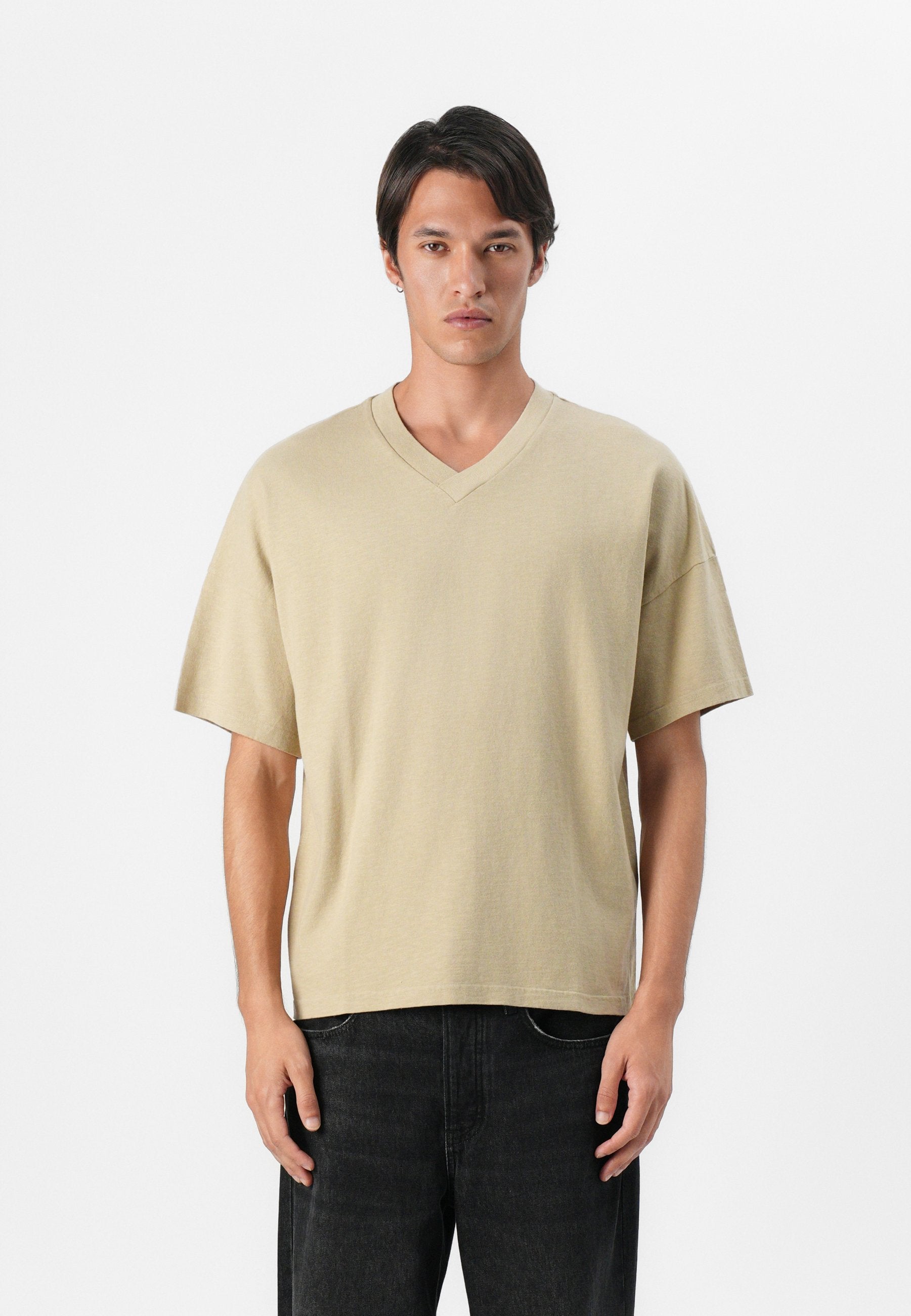 Beige T-Shirt mit kurzen Ärmeln und V-Ausschnitt aus weicher Baumwolle in lockerer Passform, kombiniert mit dunkelblauen Jeans. Schlichtes Design, keine sichtbaren Logos.