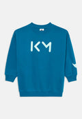 Teal Sweatshirt mit langen Ärmeln, gerippten Bündchen und Rundhalsausschnitt. Auf der Vorderseite befinden sich die Buchstaben "KM" in Hellblau und ein Logo-Akzent auf dem Ärmel.