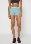 Frau trägt hellblaue Nike Pro Sportshorts und schwarzen bauchfreien Top und steht vor einem einfarbigen weißen Hintergrund.