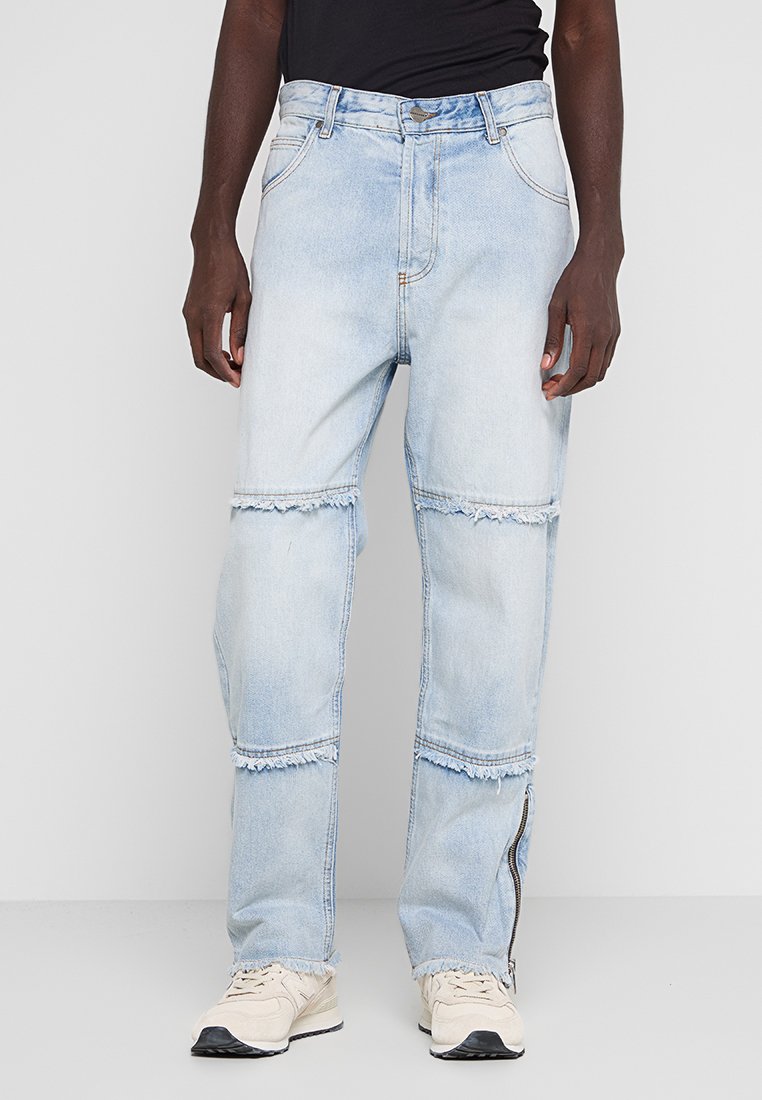 Hellblaue Jeanshose mit lockerer Passform, fransigen Details an den Knien, Fronttaschen und einem Reißverschluss am Knöchel.