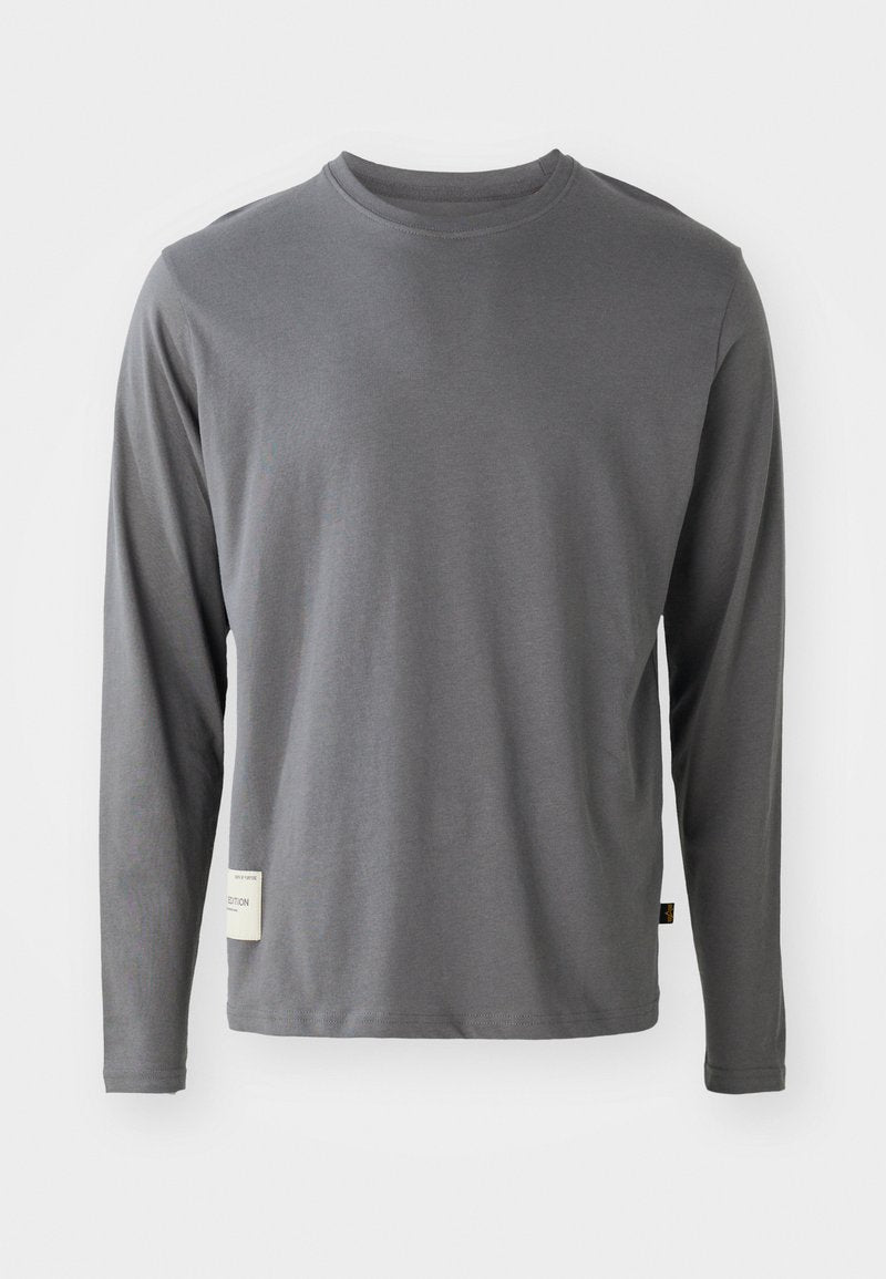 Langärmliges graues T-Shirt aus weichem Stoff; runder Ausschnitt; dezente Nahtdetails; Etikett auf der unteren linken Seite mit Text.