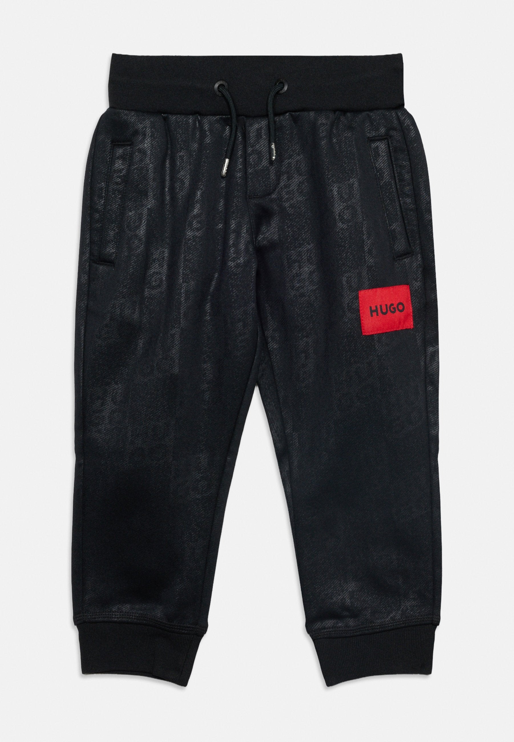Schwarze Sweatpants mit Kordelzug, Seitentaschen, gerippten Bündchen, dezentem Strukturmuster und einem roten Patch mit der Aufschrift „HUGO“ am rechten Oberschenkel.