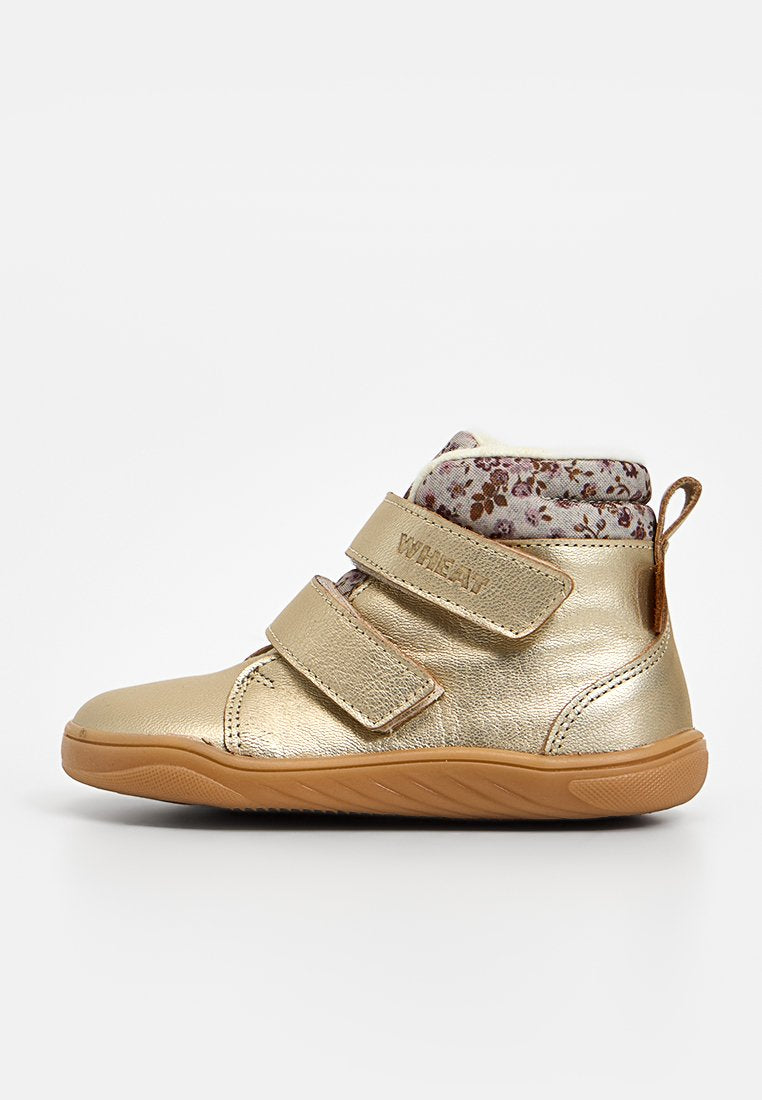 Goldener, metallischer Baby-Stiefel mit floral gemustertem Stoff am Kragen, zwei verstellbaren Klettverschlüssen und einer Gummisohle. Glatte Textur.