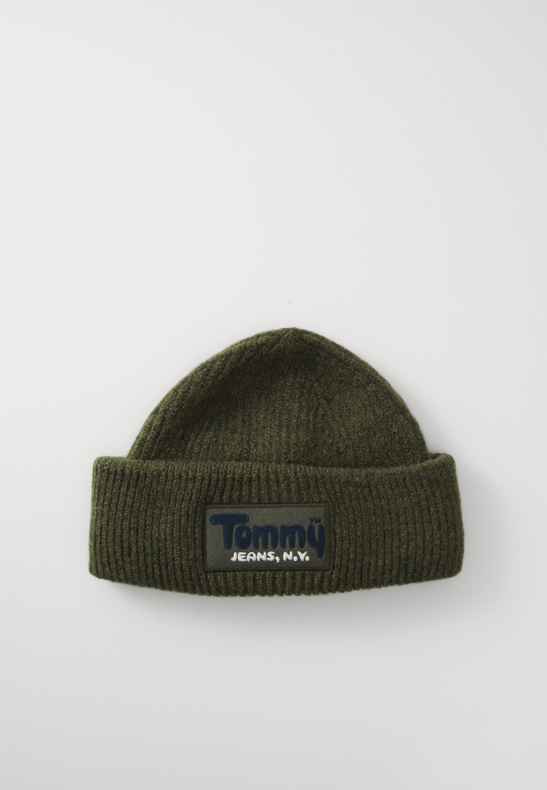 Dunkelgrüne gerippte Strickmütze mit umgeschlagenem Rand und rechteckigem Patch mit der Aufschrift "Tommy Jeans, N.Y." auf weißem Hintergrund.