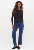 Schwarzes Langarmoberteil mit enganliegendem Design, kombiniert mit blauen geraden Jeans. Das Modell trägt schwarze Slipper und präsentiert einen lässigen Look.