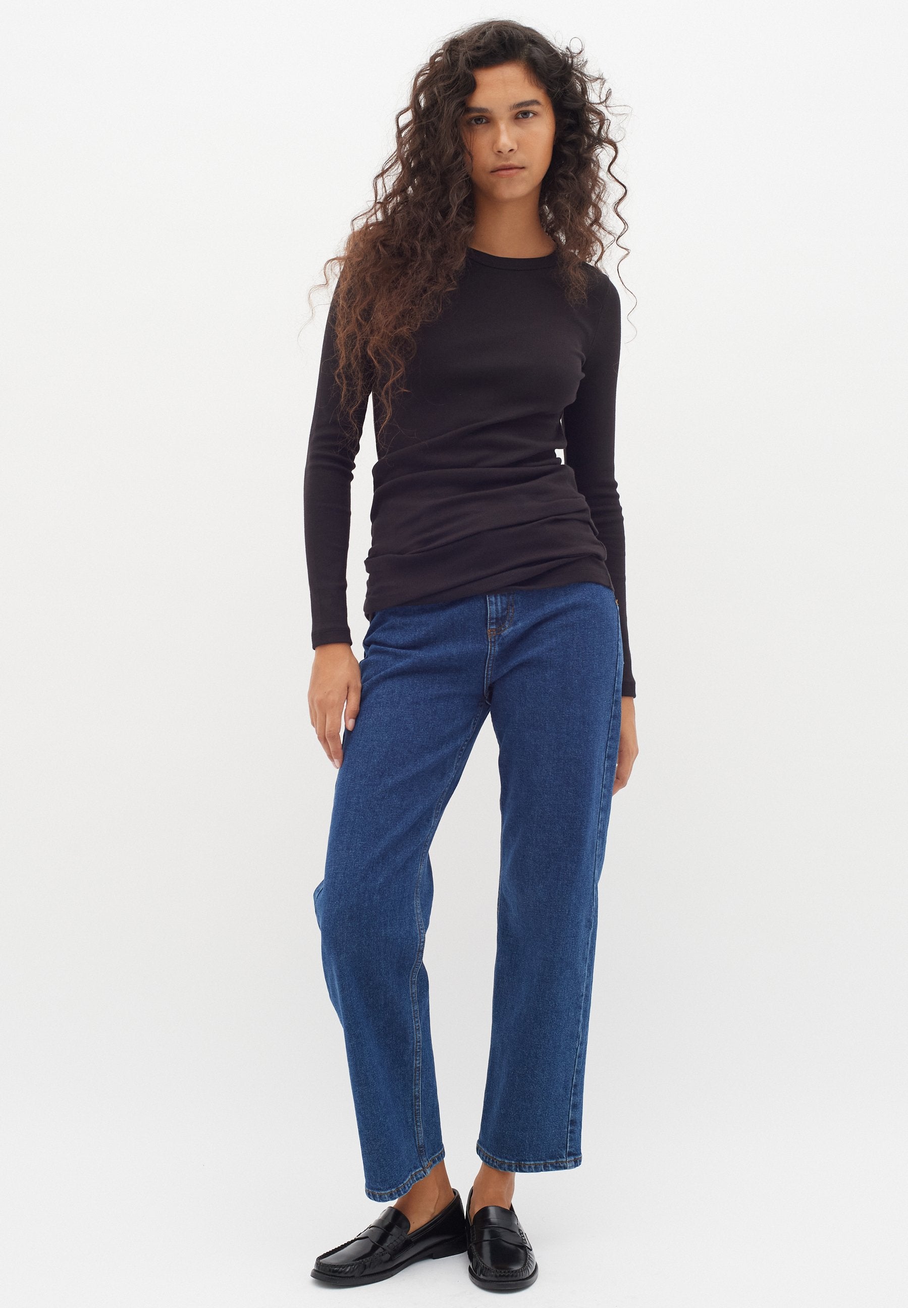 Schwarzes Langarmoberteil mit enganliegendem Design, kombiniert mit blauen geraden Jeans. Das Modell trägt schwarze Slipper und präsentiert einen lässigen Look.