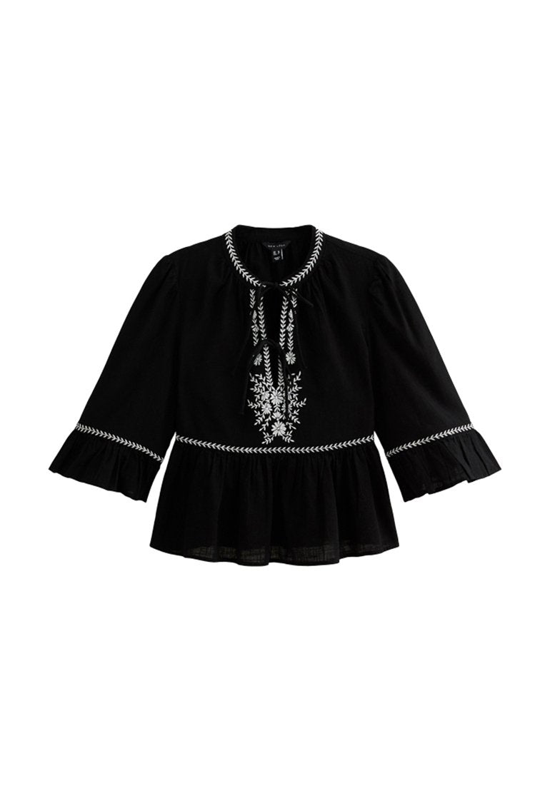 Schwarze Bluse mit weit ausladenden Ärmeln, Rüschensaum und weißer Blumenstickerei. Verfügt über einen Bindebandverschluss am Hals und einen strukturierten Stoff.