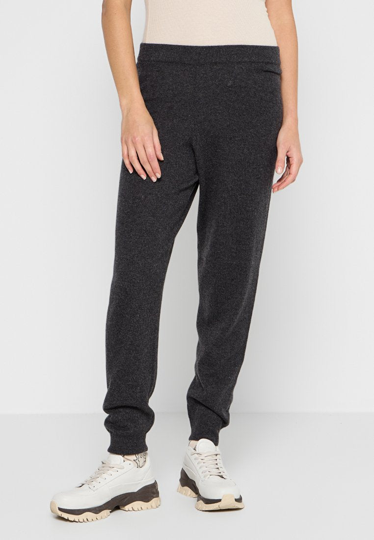 Dunkelgraue Jogginghosen aus einem weichen Stoff, mit einem elastischen Bund und einer zulaufenden Beinform, kombiniert mit weißen und grauen Sportschuhen.