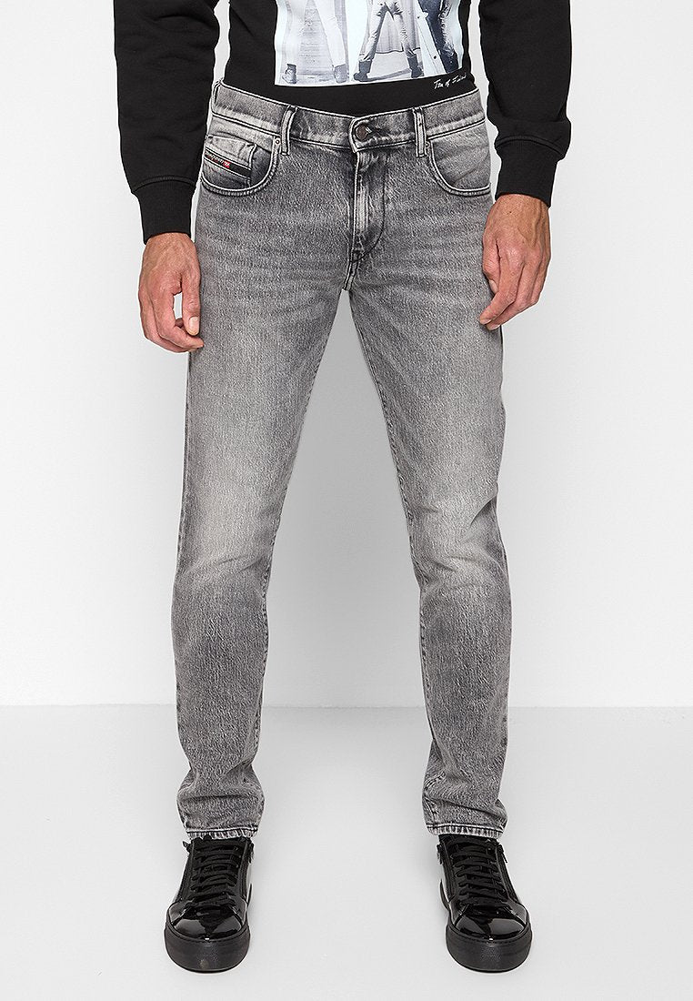 Graue Jeans aus Denim mit geradem Schnitt, die dezente Verblassungen, ein Fünf-Taschen-Design und schwarze Nähte aufweisen. Getragen mit schwarzen Sneakers.