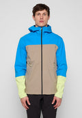 Mann trägt eine blau-beige-hellgelbe Kapuzenjacke mit Reißverschluss und vorderen Reißverschlusstaschen, steht vor einem schlichten grauen Hintergrund.