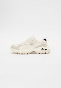 Sneaker mit einem hellbeigen und grauen Netzoberteil, strukturierten Überzügen, einer klobigen weißen Sohle und schwarzen Details an der Ferse.