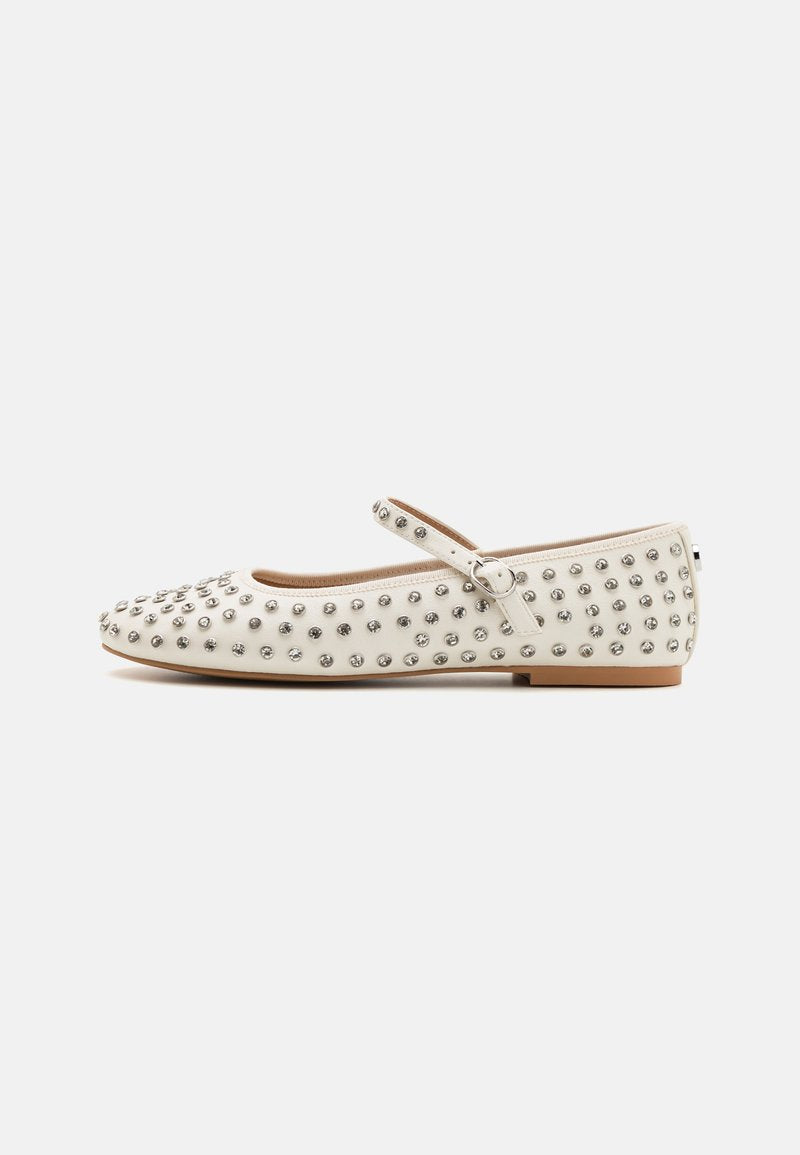 Weiße flache Schuhe mit einer abgerundeten Spitze, verziert mit silbernen Nieten, ausgestattet mit einem dekorativen Riemen über dem Rist und einem niedrigen Absatz.