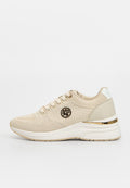 Beige gestrickter Sneaker mit weißer Sohle, goldfarbenem Akzent an der Ferse, Schnürung vorne und rundem Logo-Emblem an der Seite.