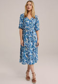 Blaues Blumenkleid in Midilänge mit kurzen Puffärmeln, V-Ausschnitt und Bindeband in der Taille. Das Kleid besteht aus einem gemusterten Stoff in Blau- und Weißtönen.
