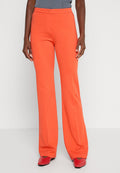 Leuchtend orangefarbene Hosen mit glatter Textur, ausgestelltem Design, mittelhohem Bund und geradem Schnitt. Kombiniert mit roten Schuhen.