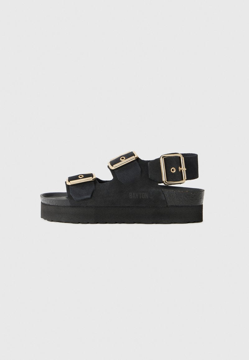 Schwarze Wildleder-Sandale mit drei breiten Riemen, von denen jeder mit einer goldenen Schnalle versehen ist. Dicke schwarze Sohle und der Text "BAYTON" ist an der Seite geprägt.
