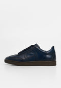 Marineblaue Ledersneaker mit glatter Oberfläche, runder Zehenpartie, Schnürdesign und kontrastierender brauner Gummisohle; verfügt über ein dezentes, eingeprägtes Logo.