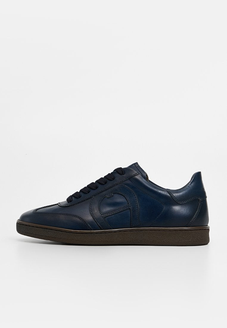 Marineblaue Ledersneaker mit glatter Oberfläche, runder Zehenpartie, Schnürdesign und kontrastierender brauner Gummisohle; verfügt über ein dezentes, eingeprägtes Logo.