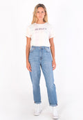 Hellblaue T-Shirt mit leichtem Batikmuster und dem Schriftzug "HURLEY", hochgeschnittene blaue Jeans mit lockerer Passform und weiße Sneaker, die frontal vor einem weißen Hintergrund stehen.