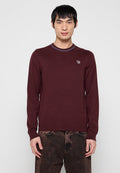 Weinroter Pullover mit langen Ärmeln, geripptem Muster und Rundhalsausschnitt, ausgestattet mit einem kleinen gestickten Design auf der Brust und kontrastierenden Nahtdetails am Kragen.