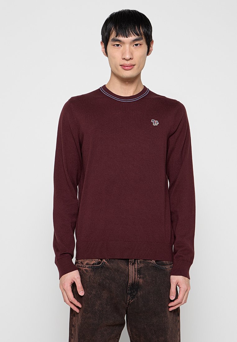 Weinroter Pullover mit langen Ärmeln, geripptem Muster und Rundhalsausschnitt, ausgestattet mit einem kleinen gestickten Design auf der Brust und kontrastierenden Nahtdetails am Kragen.