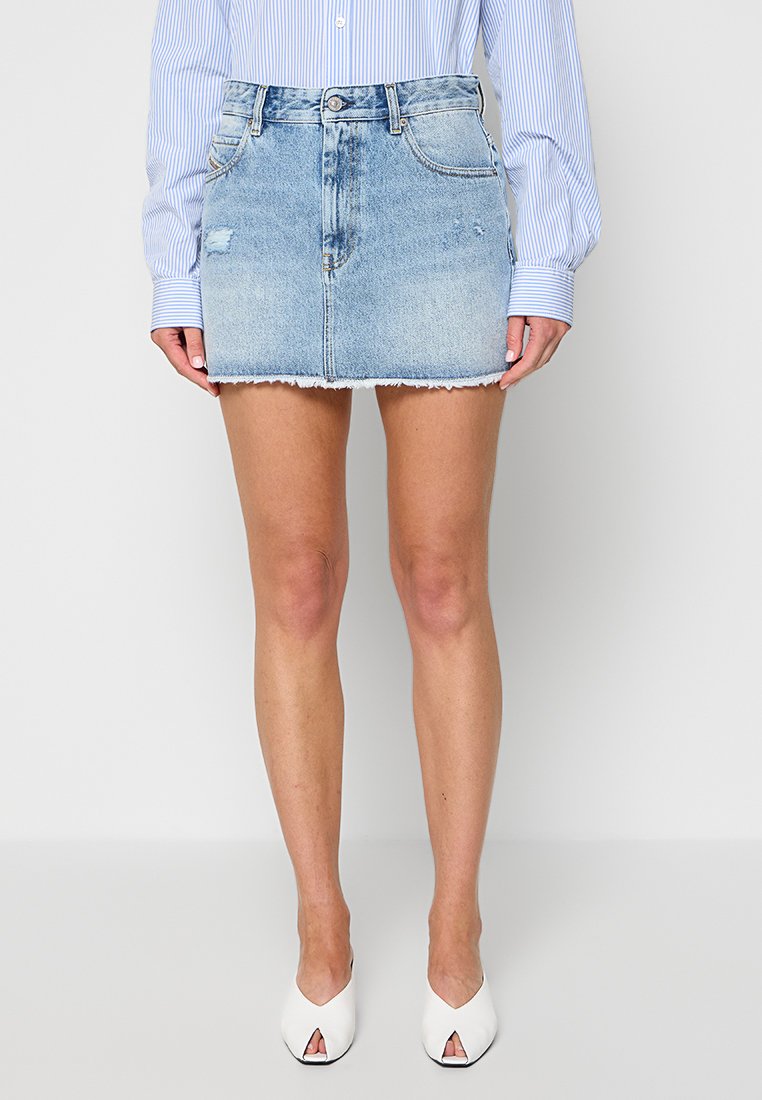 Frau trägt ein hellblau gestreiftes Langarmshirt, einen hellblauen Jeans-Minirock mit ausgefranstem Saum und weiße offene Mules.