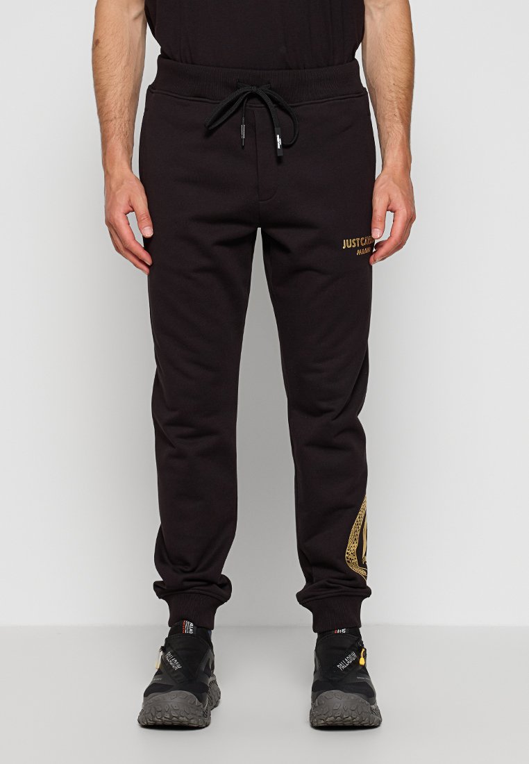 Schwarze Sweatpants aus weichem Stoff, mit einem verstellbaren Bund, Seitentaschen und goldenen Branding-Akzenten am linken Bein.