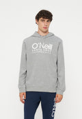 Junger Mann mit lockigem Haar, der einen grauen O’Neill-Hoodie und marineblaue Hose mit O’Neill-Logo auf einem Bein trägt, steht vor einem schlichten Hintergrund.
