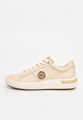 Beige Sneaker mit niedrigem Schaft, weißen Schnürsenkeln, strukturiertem Leder, goldfarbenem Emblem an der Seite und dicker weißer Sohle mit beigem Akzent.