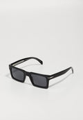 Schwarze rechteckige Sonnenbrille mit dunklen Gläsern, glänzendem Kunststoffrahmen und silbernen Akzenten an den Schläfen, ausgestattet mit einer strukturierten Oberfläche an den Bügeln.
