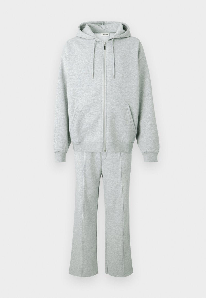 Grauer Kapuzenpullover und passende Jogginghose aus weichem Stoff, mit durchgehendem Reißverschluss vorne, Kapuze und Seitentaschen. Die Hose hat gerade Beine mit Nähten.