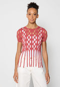 Rotes Strickoberteil mit offenen ovalen Ausschnitten, kurzen puffärmel und einem geschichteten Design mit weißem Unterlayer. Kombiniert mit hellen Hosen.
