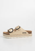 Beige Rutschsandalen aus strukturiertem Material, mit zwei schwarzen sechseckigen Schnallen, einem Korkfußbett und einer geflochtenen Espadrille-Sohle.