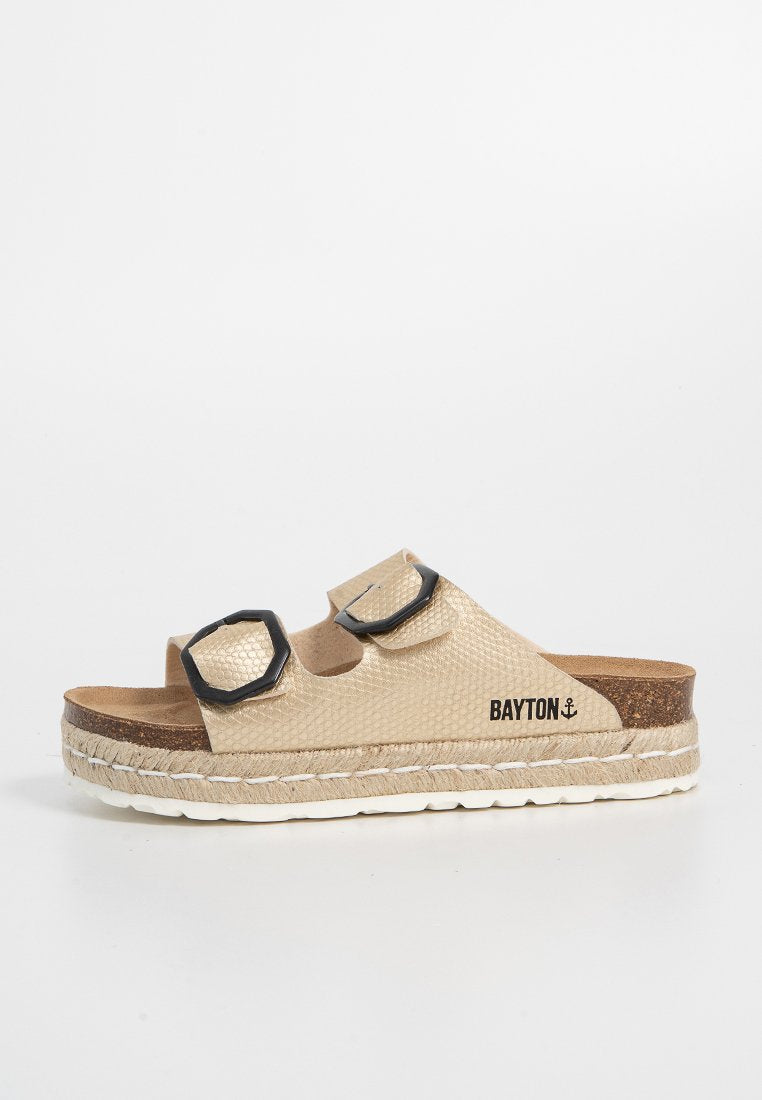 Beige Rutschsandalen aus strukturiertem Material, mit zwei schwarzen sechseckigen Schnallen, einem Korkfußbett und einer geflochtenen Espadrille-Sohle.